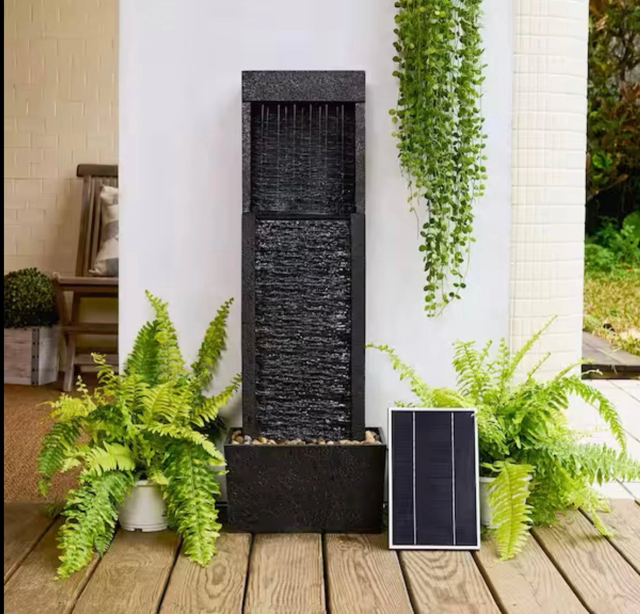 A 38-inch solar-powered gray slate waterfall fountain with LED lights, set in an outdoor garden area with surrounding plants and grass.