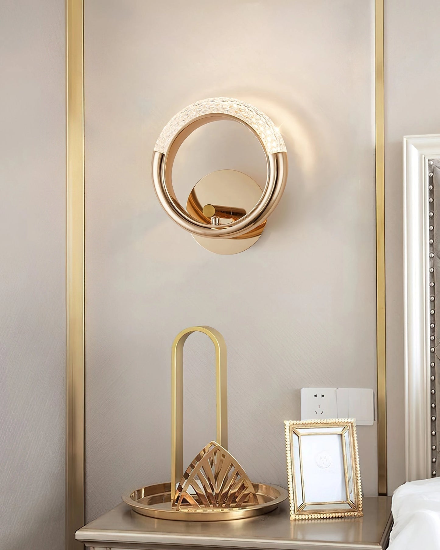 Luxurious metallic rotatable wall lamp with an adaptable angle, positioned near a gold-framed mirror in a modern interior design setting featuring wooden elements and a chair.