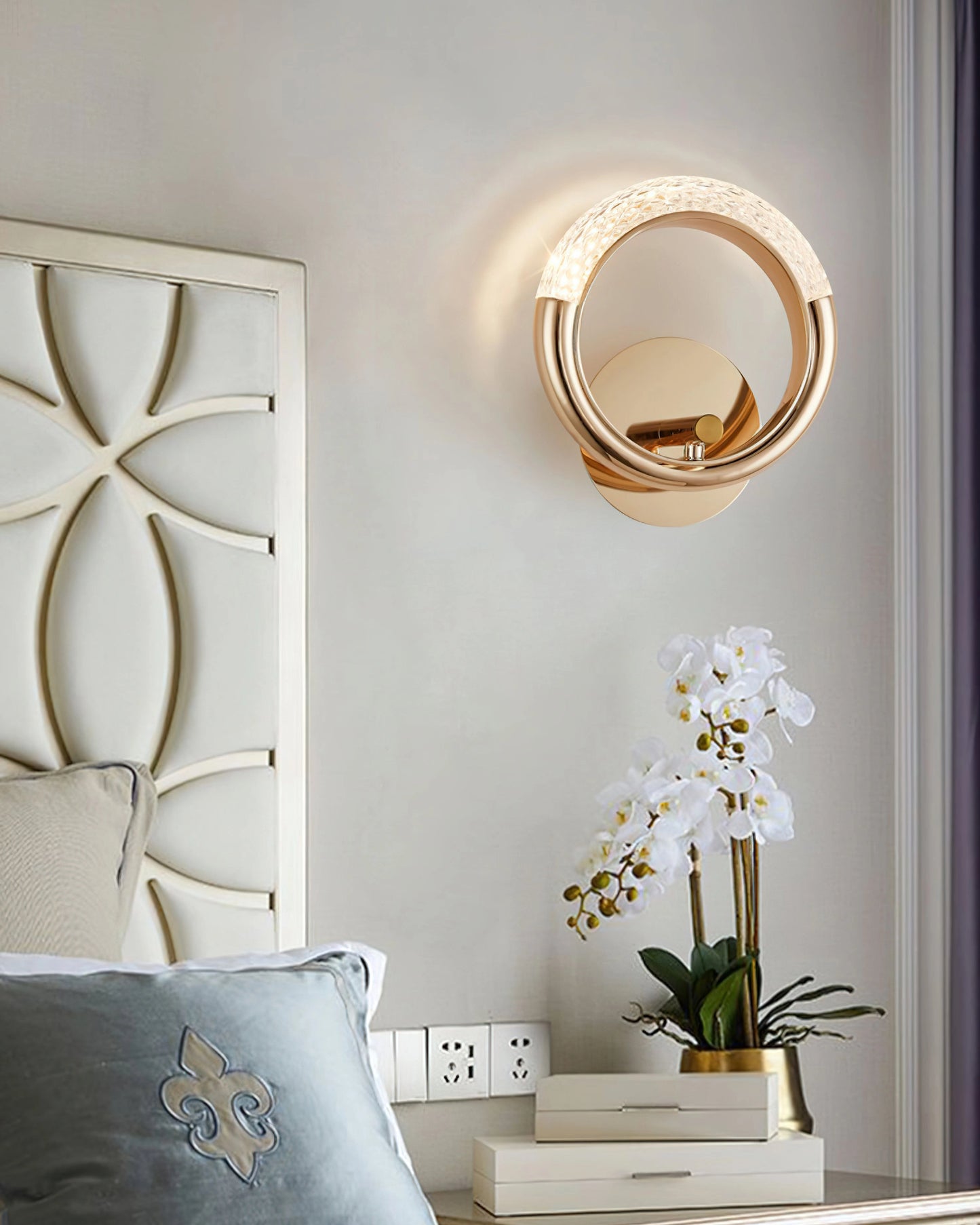 Luxurious metallic adaptable angle rotatable wall lamp illuminating a modern interior with houseplant in flowerpot and white textile elements.