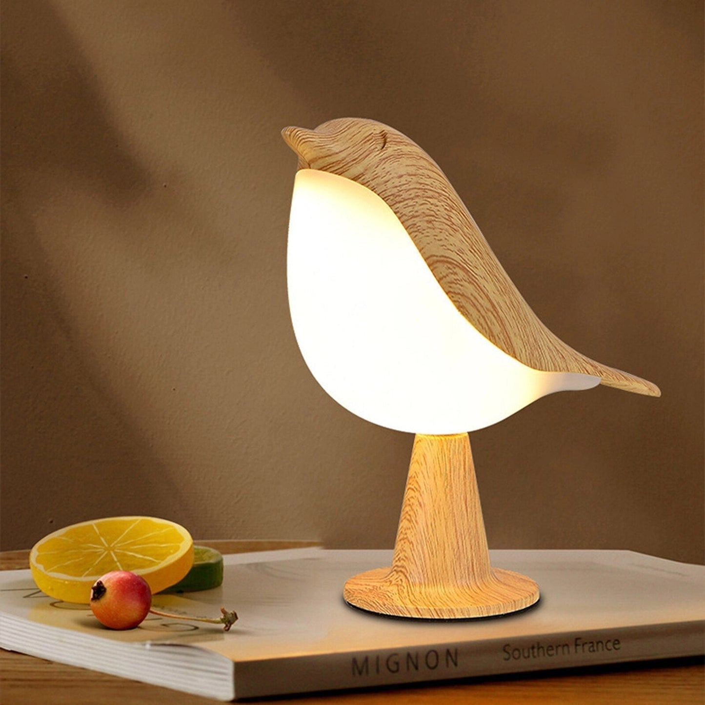 A dimmable LED cordless bird-shaped table lamp on a wooden nightstand surrounded by tableware, citrus fruits, and decorative serveware.