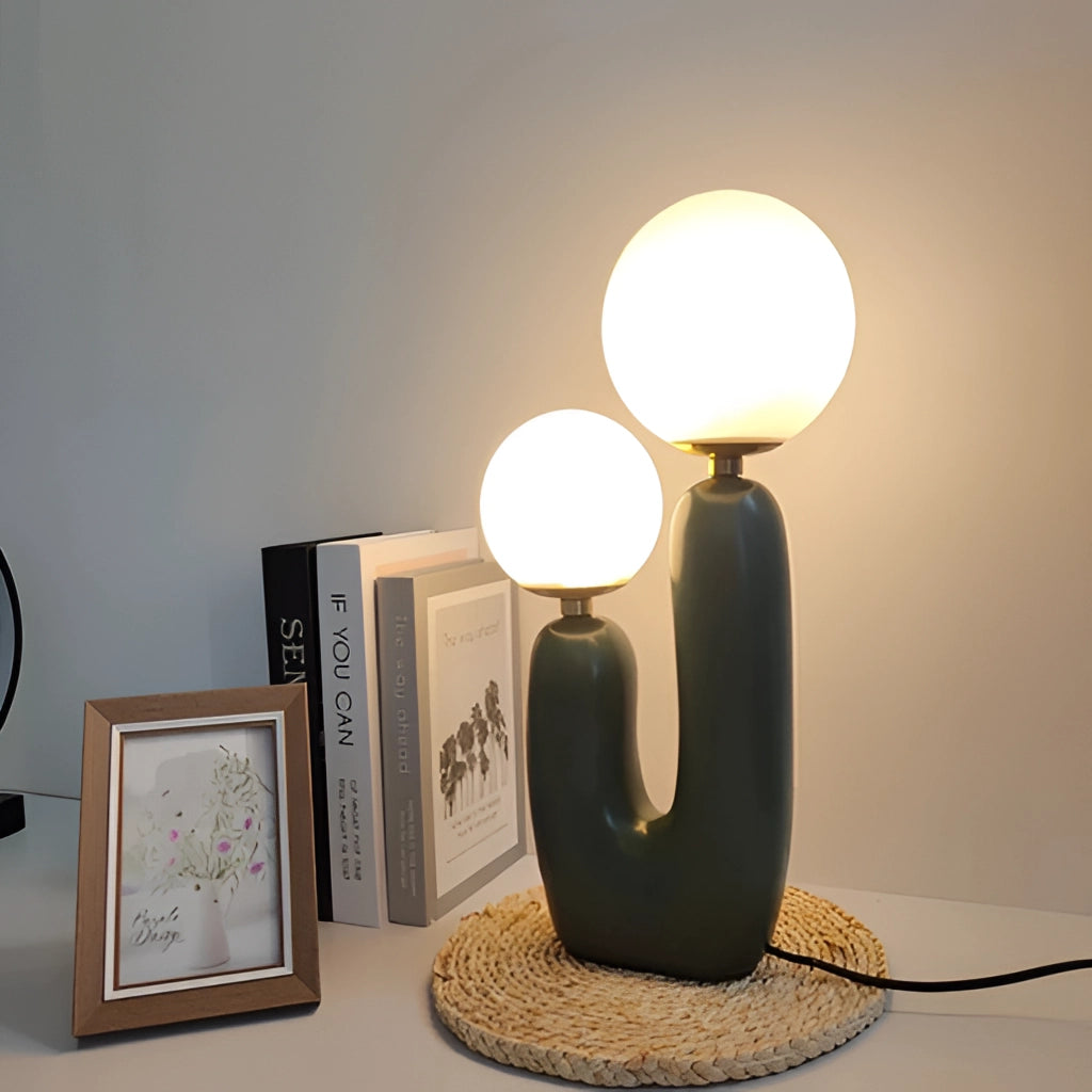 Cactus design table lamp with milk glass globes and LED innovation on a wooden table, surrounded by picture frames and other furniture.