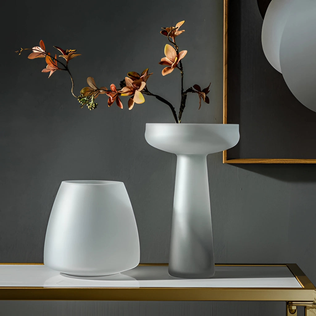 A coffee-colored frosted glass vase on a table with interior design elements in the background.