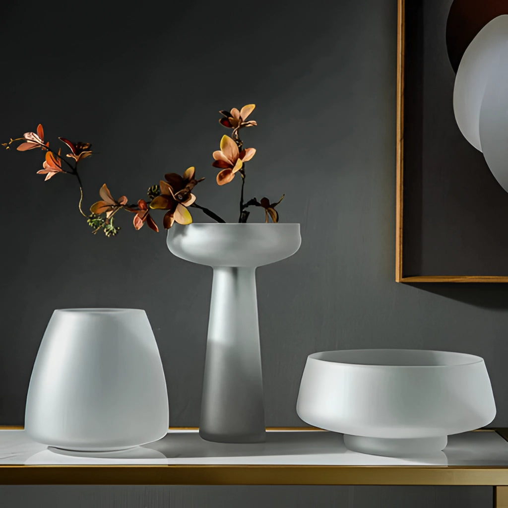 Coffee-colored frosted glass vase on a table with houseplants and interior decor in the background.