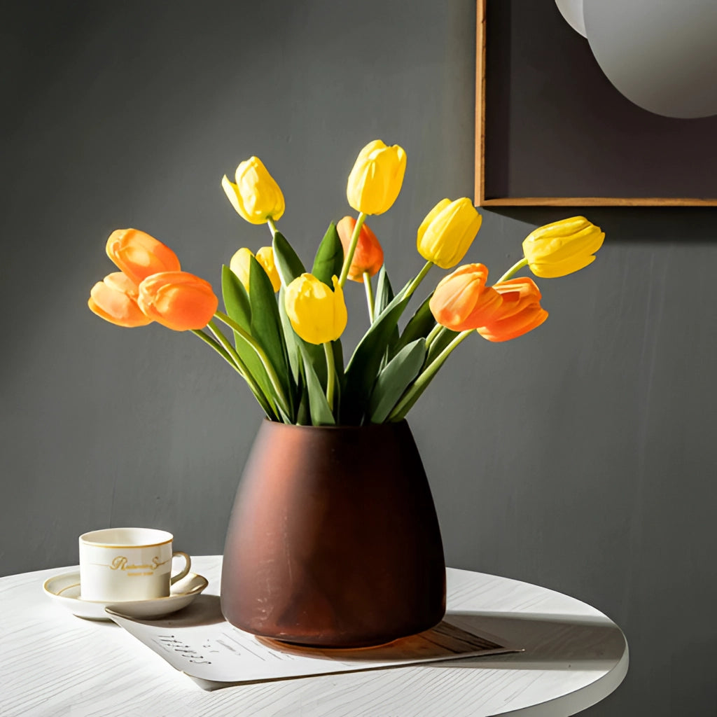 A coffee-colored frosted glass vase filled with orange flowers on a table, enhancing the interior design.