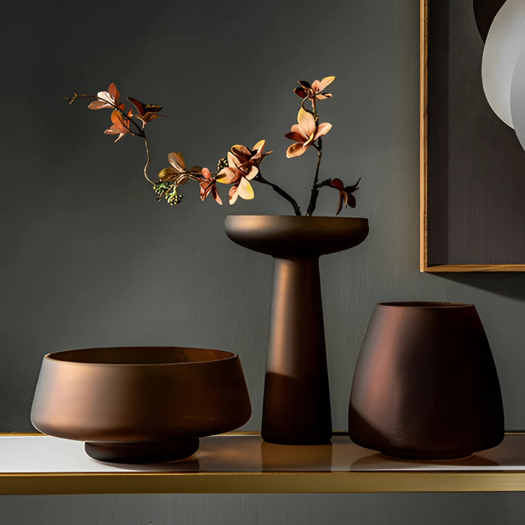 A coffee-colored frosted glass vase on a wooden table with a houseplant and twigs inside, set in a stylish interior design.