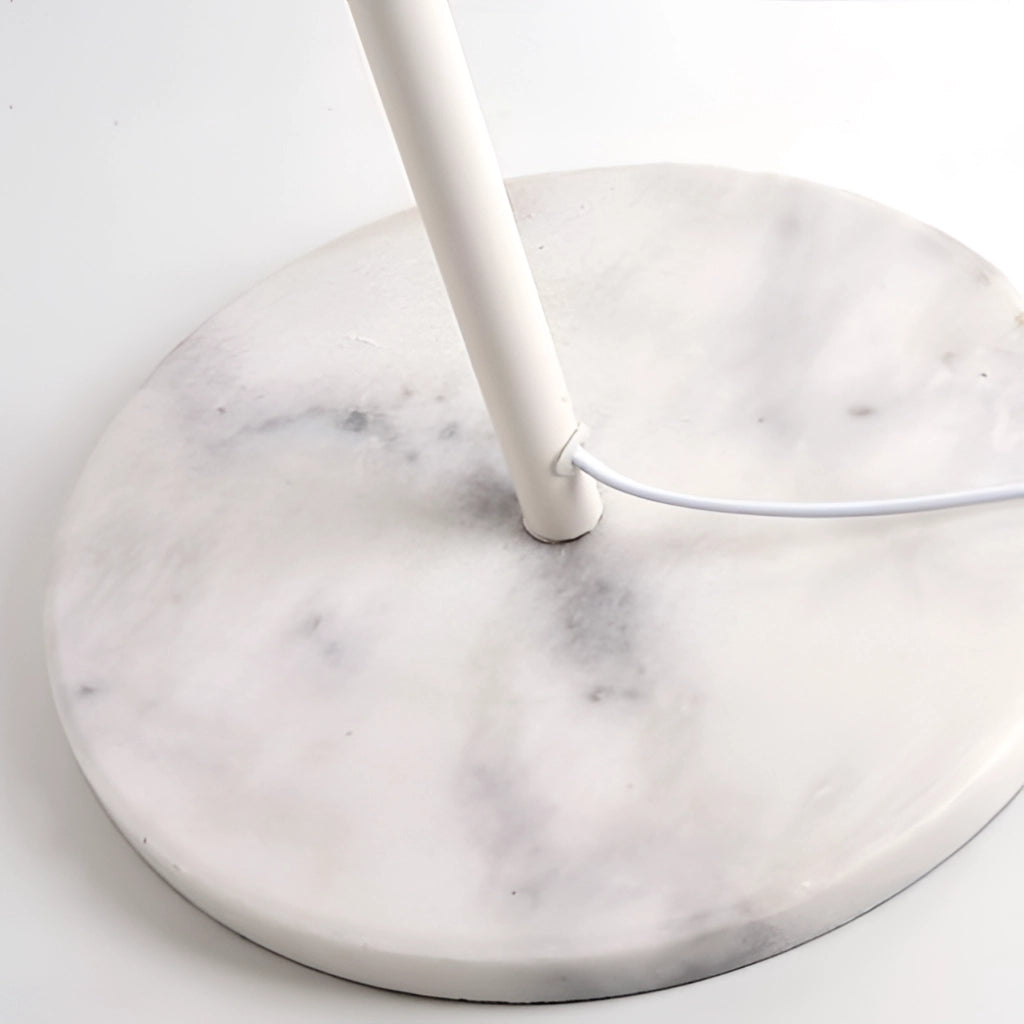 Floor lamp with a sleek metal pole and a round marble base, standing in a modern kitchen near various utensils and dishes.