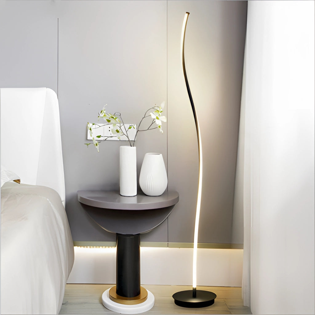 Black floor lamp with remote control and 3 light temperatures placed next to a table with a vase and a plant in a modern interior design setting.