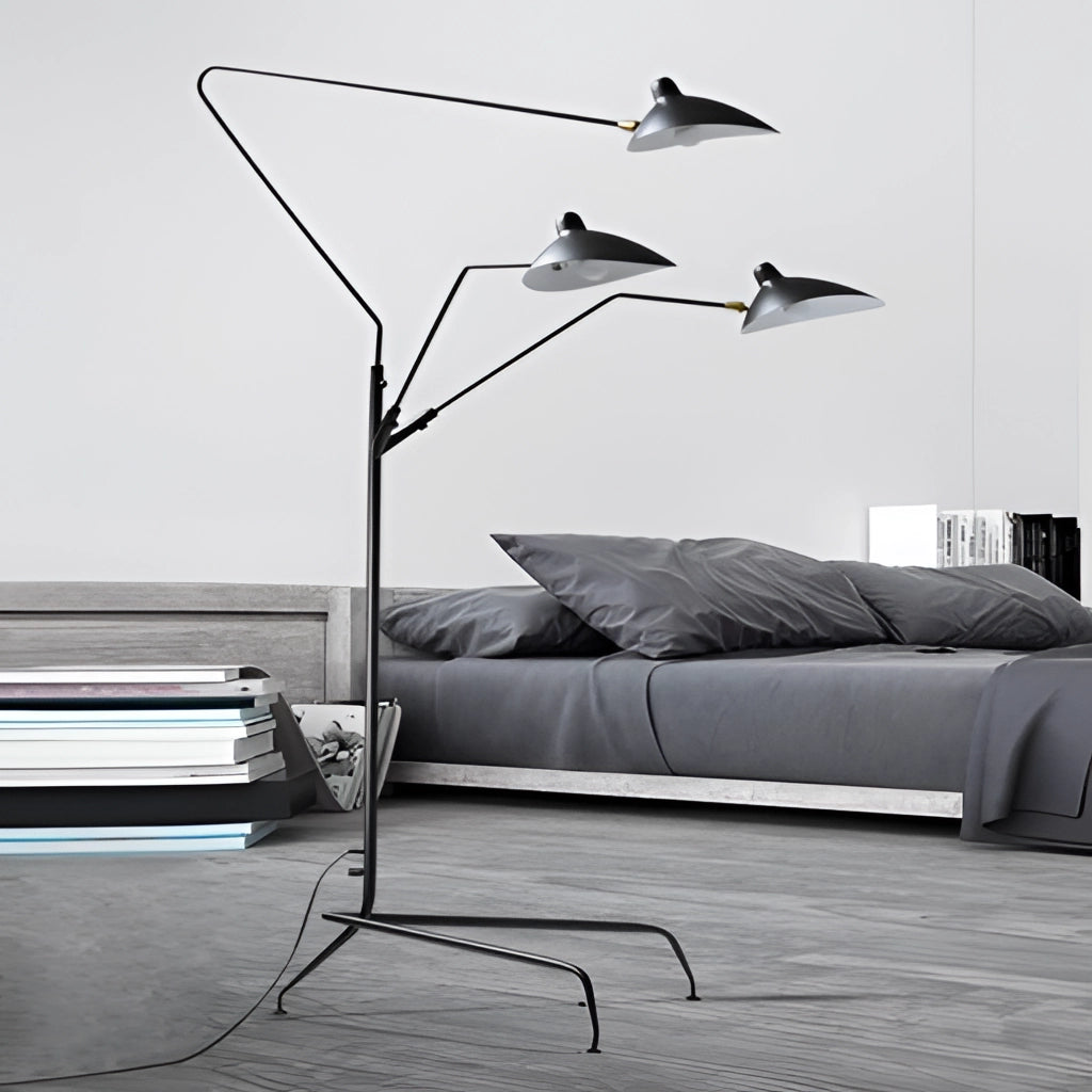A modern floor lamp with a tripod base and directional light, positioned next to a grey couch in a comfortable living room setting.