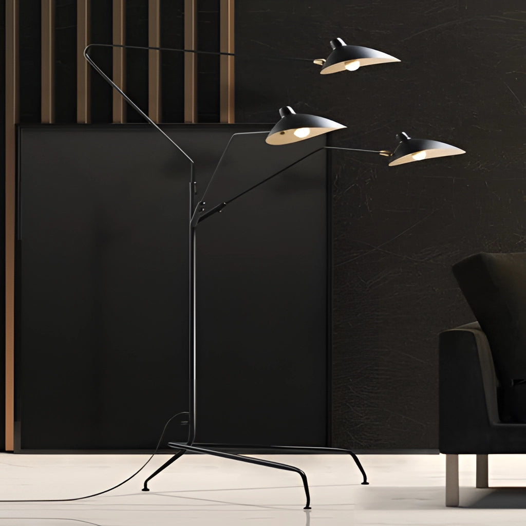A stylish floor lamp with a tripod base and directional light, standing next to a modern chair on wooden flooring, set against a dark background with minimalist art.
