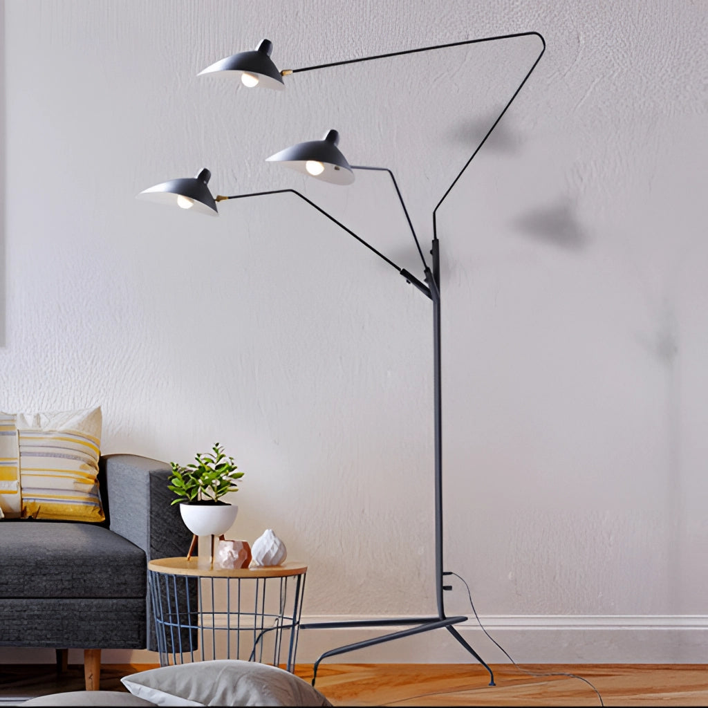 A stylish floor lamp with a tripod base and directional light, placed next to a grey flowerpot with a houseplant on a hardwood floor.
