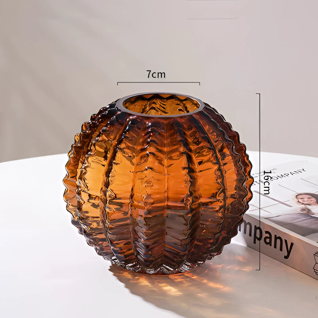 Small brown glass cactus vase with artistic design, surrounded by various decorative elements including lanterns, lamps, wood, and metal accents.