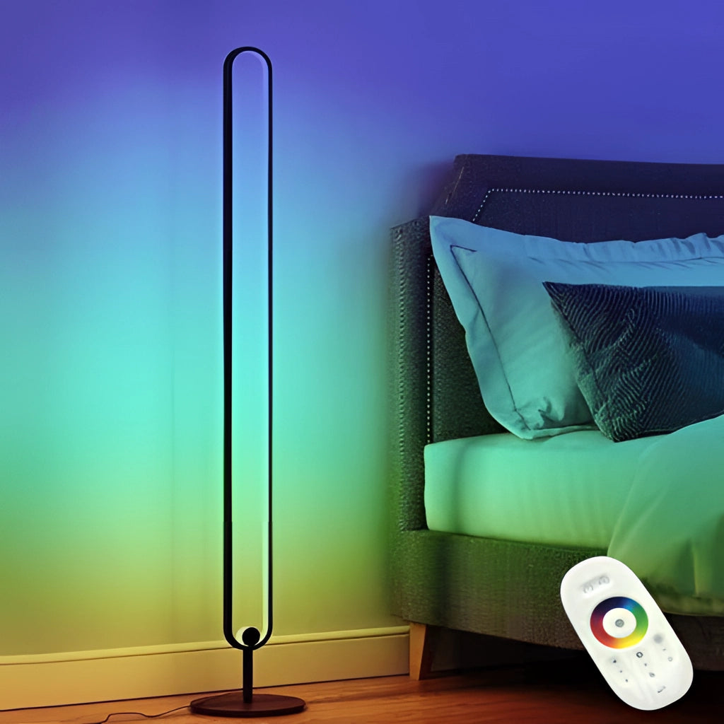 A stylish LED floor lamp with RGB multicolor and warm white lighting, placed in a cozy interior setting with pillows, showcasing its sleek rectangular design and soft orange glow.