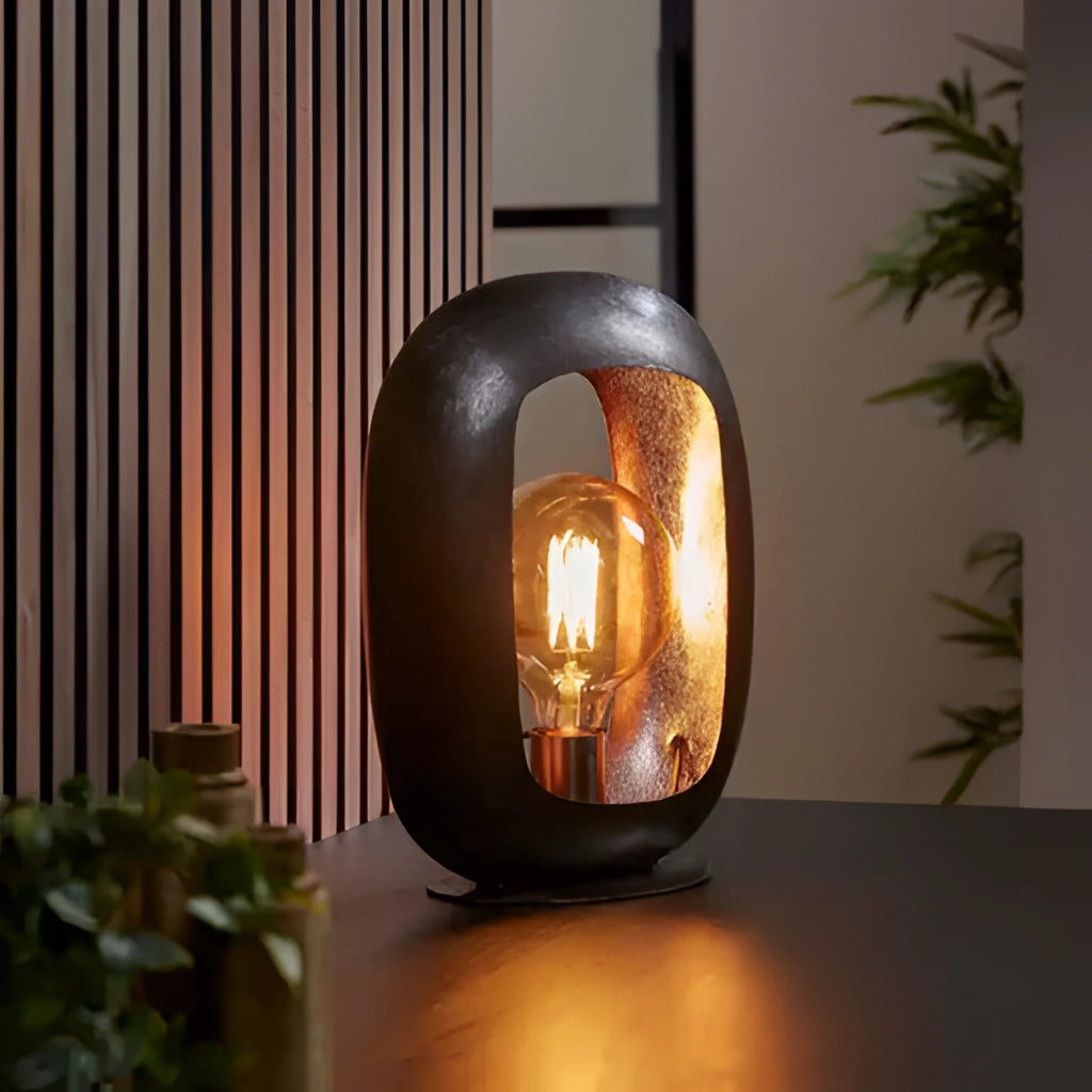 Vintage style table lamp made of metal with amber light, placed on a wooden surface next to a plant.
