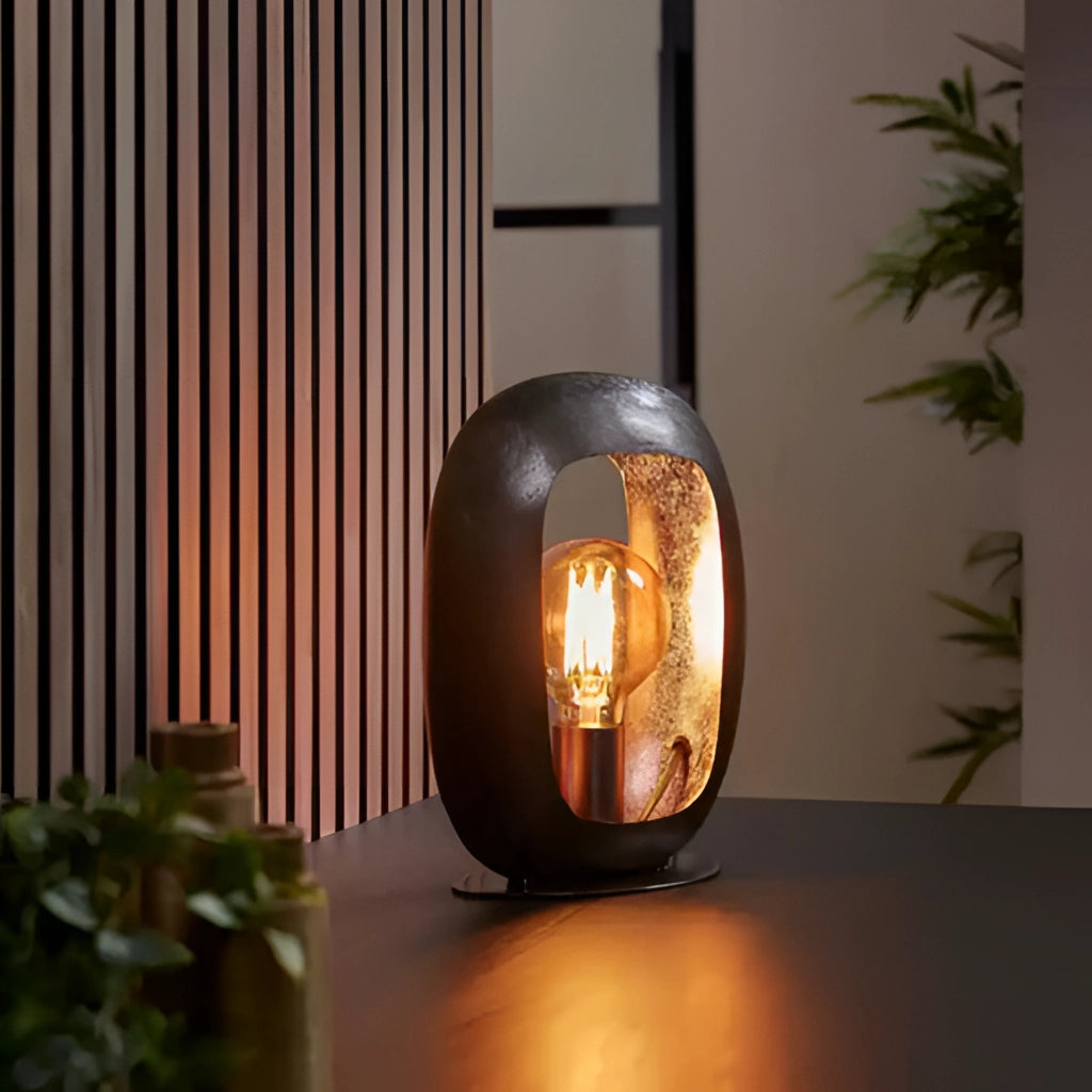 Small metal crafted vintage style table lamp with amber lighting next to a potted plant on a wooden surface, featuring orange tints and interior design elements.