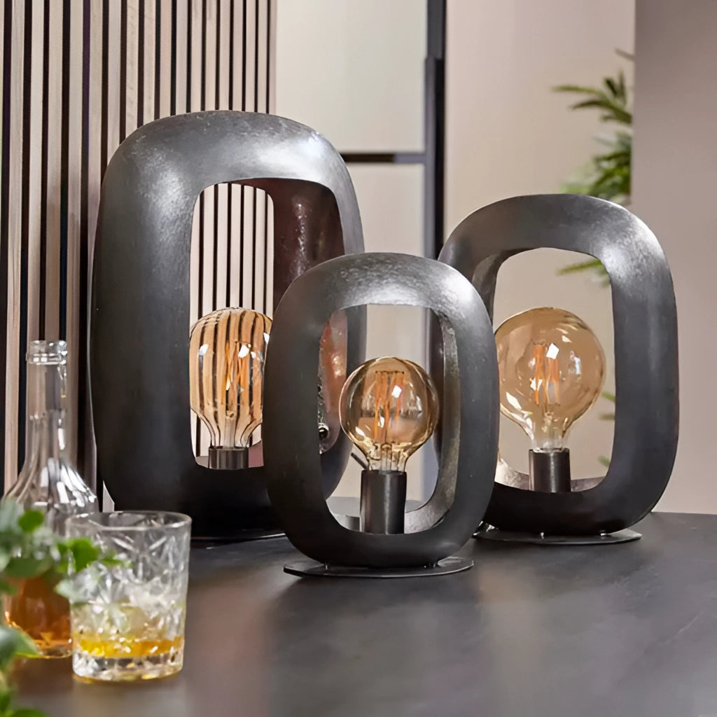 Vintage-style metal crafted table lamps on a wooden surface with glass drinkware and tableware nearby.
