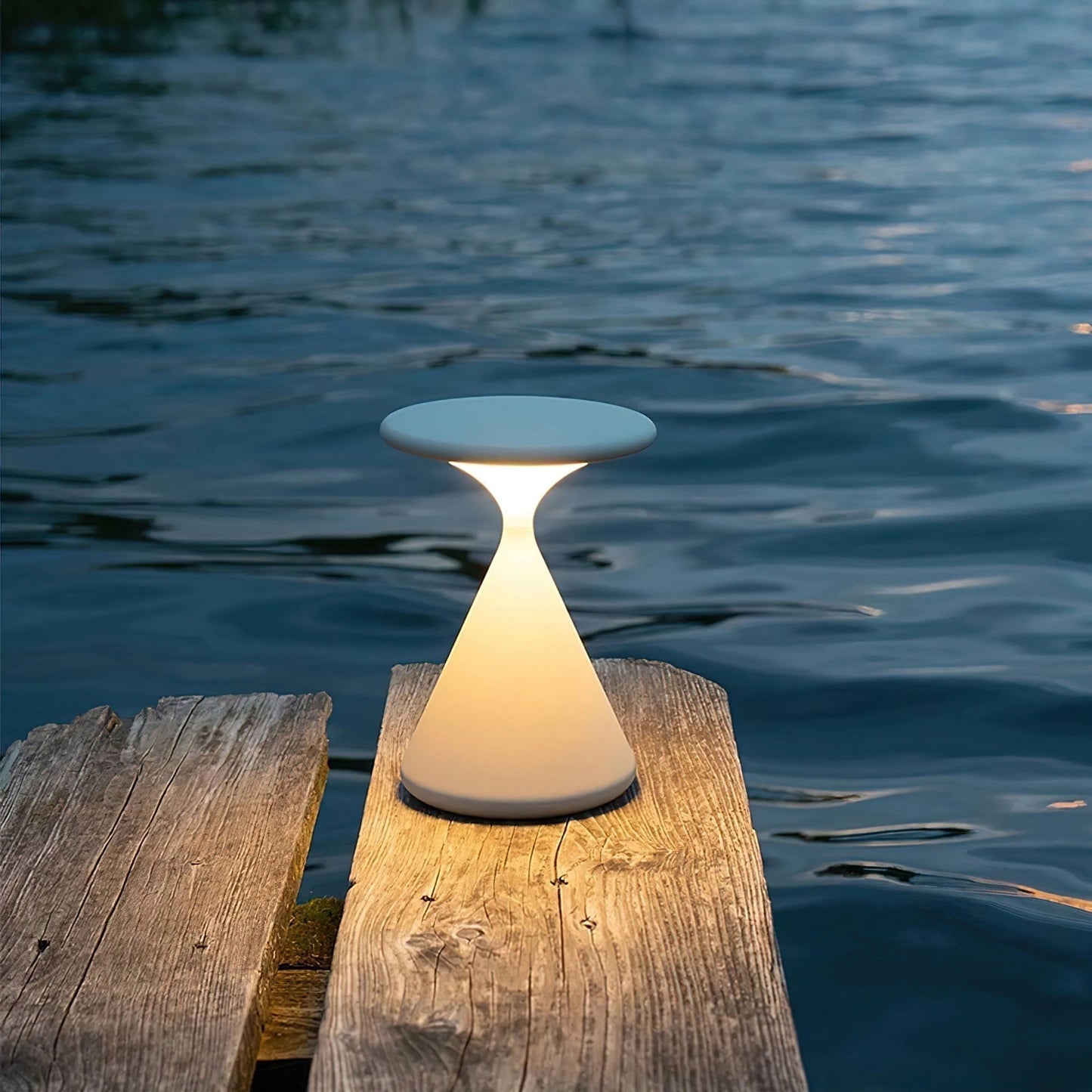 Outdoor cordless lamp named Selene placed on a wooden surface near a serene lake with a clear sky and symmetrical landscape in the background.