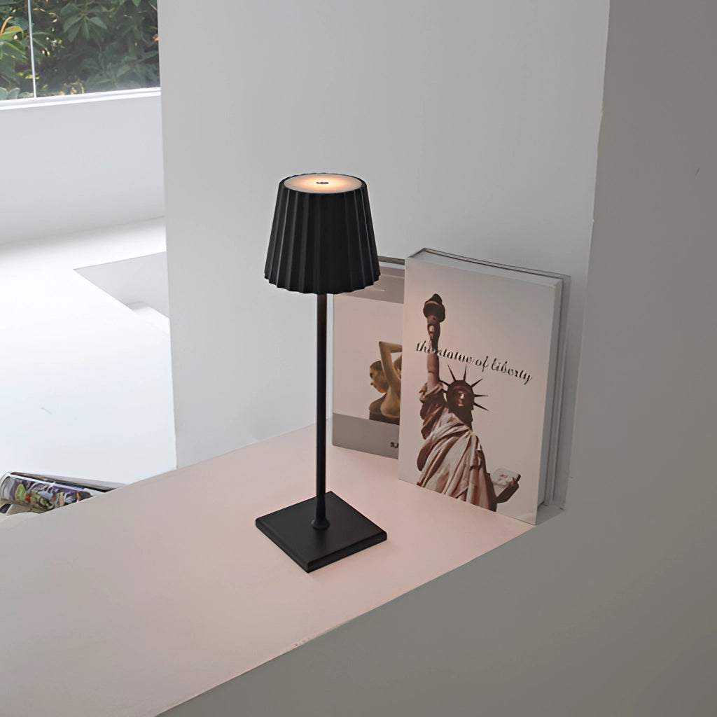 Cordless LED table lamp with stepless dimming on a wooden table, featuring a sleek grey design and modern interior decor elements in the background.