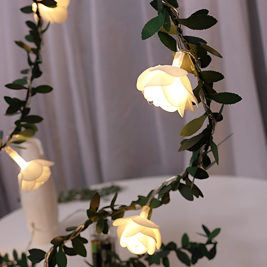 Battery-operated LED string lights designed as a garland of rose flowers with green leaves and branches, perfect for interior decoration.