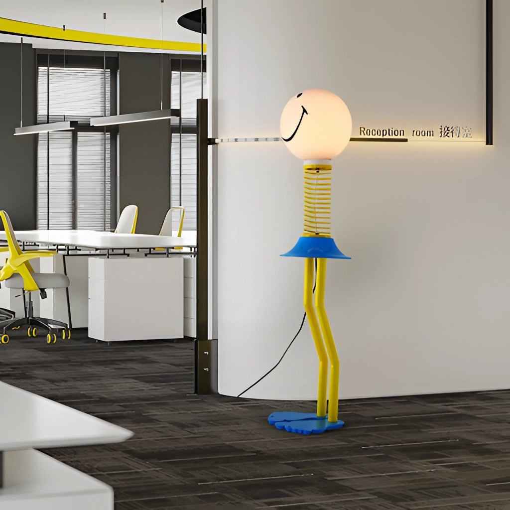 Yellow, blue, and white smiley face design floor lamp made of metal, iron, acrylic, and glass, placed in a cozy bedroom setting with wooden flooring, a window, and wall art in the background.