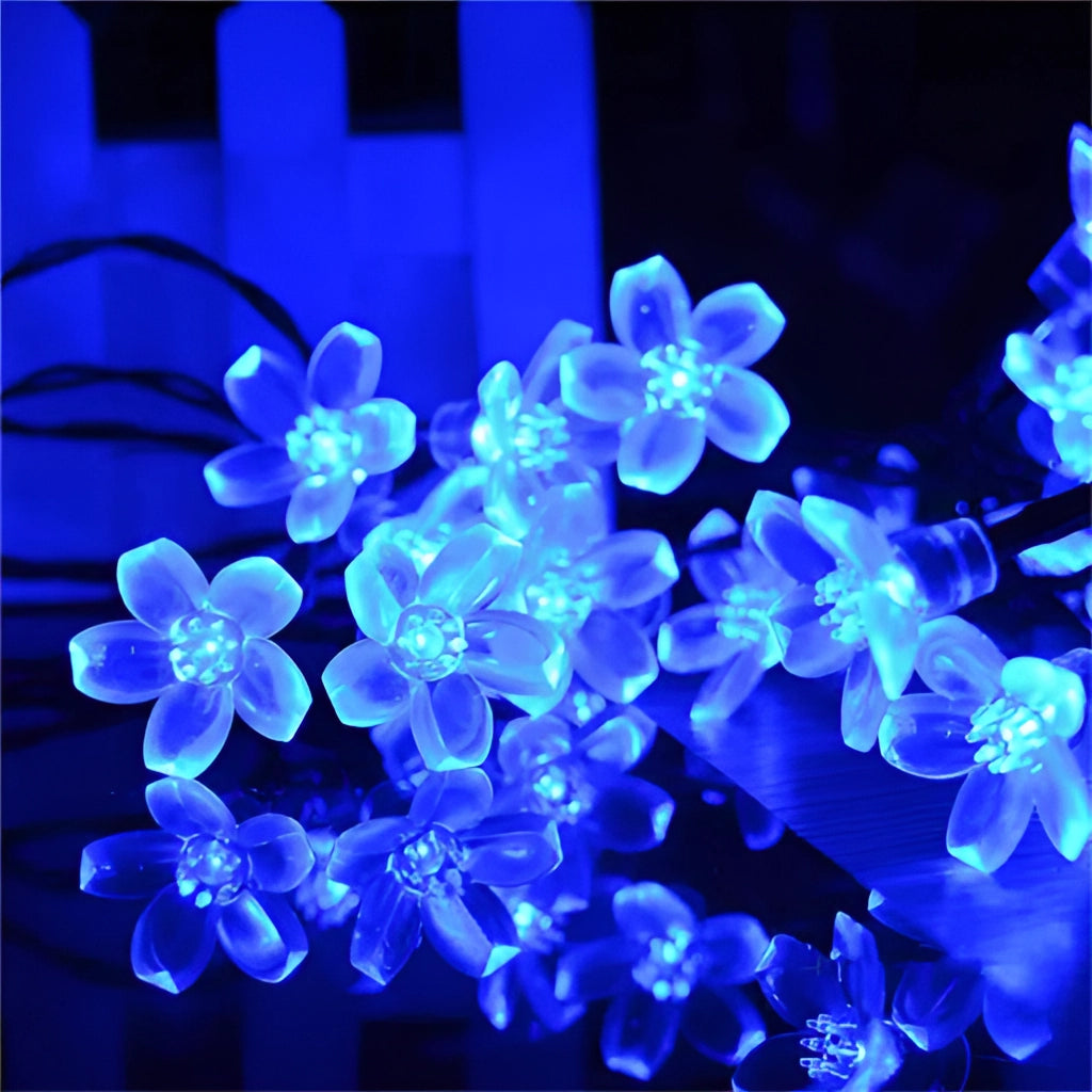 Solar Flower Garden LED Light Strips in Cherry Blue illuminating blue and purple flowers and petals at night.