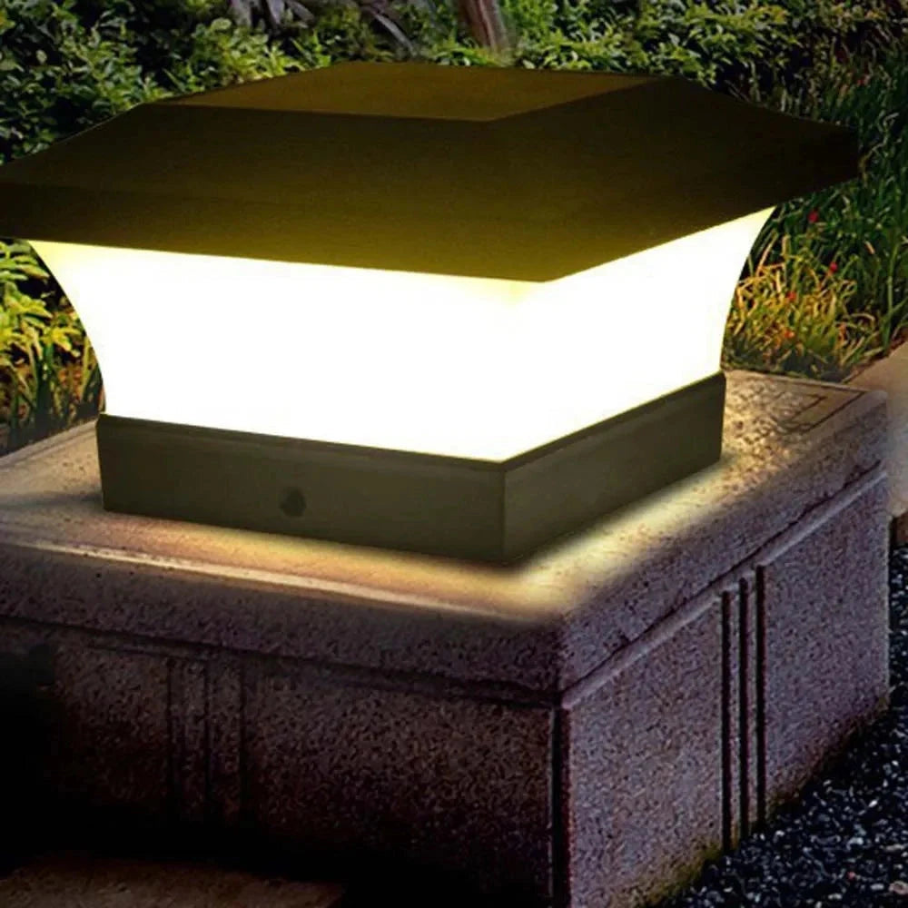Solar post cap lights illuminating an outdoor garden area at night, surrounded by grass and shrubs, with warm white light glowing from the fence posts.