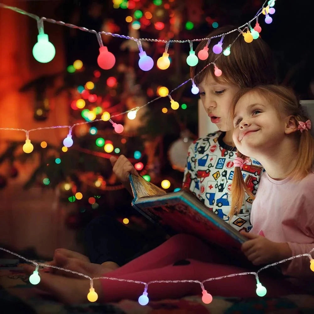 Solar powered waterproof outdoor LED string lights illuminating a garden, wrapped around a tree, creating a festive and happy atmosphere.
