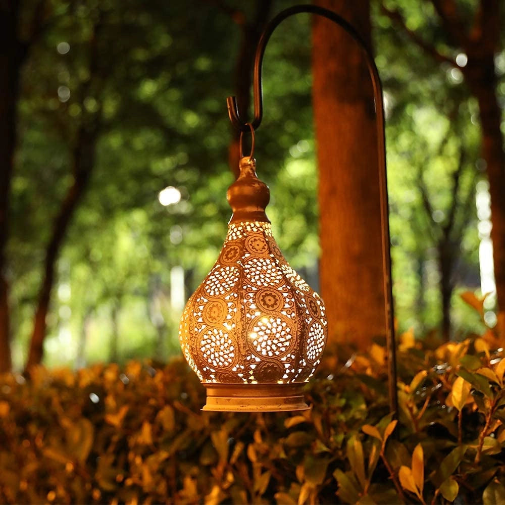 Vintage Moroccan metal lantern with amber lighting, featuring intricate ornamental designs, placed among wooden branches and grass.