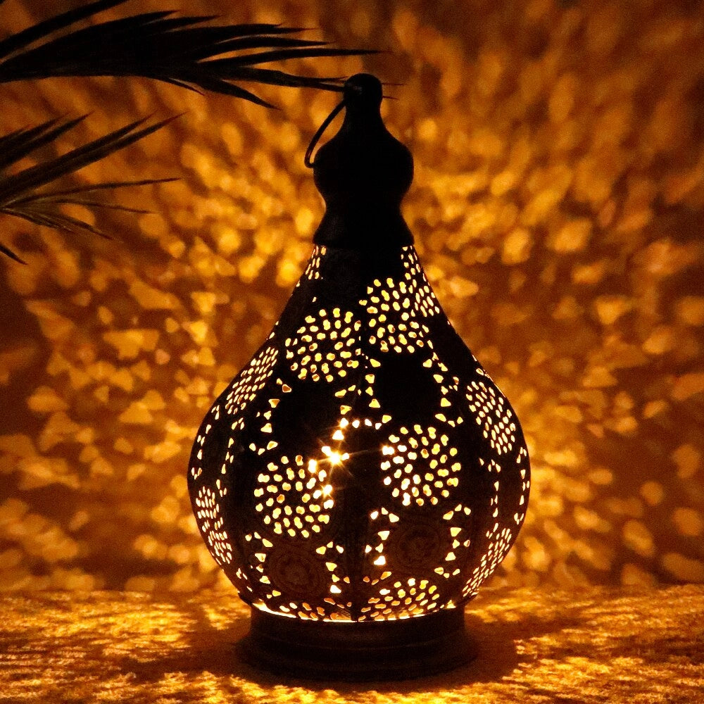 Vintage Moroccan metal lantern with intricate designs, placed on a wooden surface, surrounded by holiday ornaments and greenery.