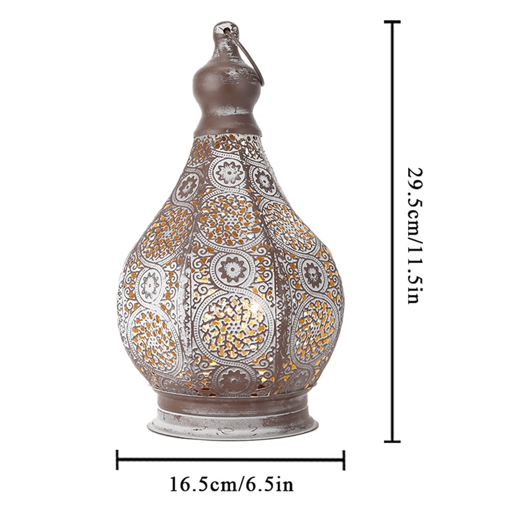 A vintage Moroccan metal lantern with intricate patterns, battery-powered, displayed on a table next to bird-themed pottery and other decorative artifacts.