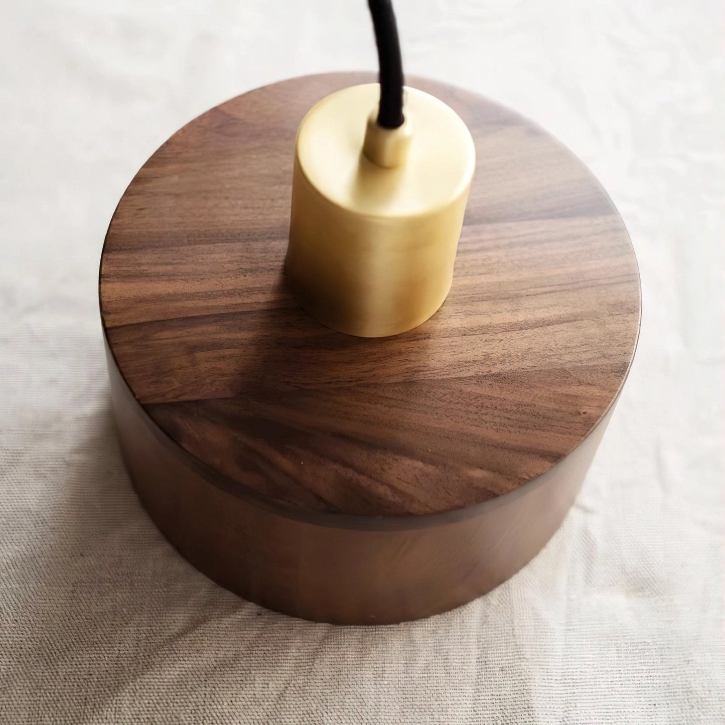 Walnut wood pendant lamp inspired by Japanese woodworking, hanging as a ceiling fixture above a table. The lamp features a circular design with a varnished hardwood finish.