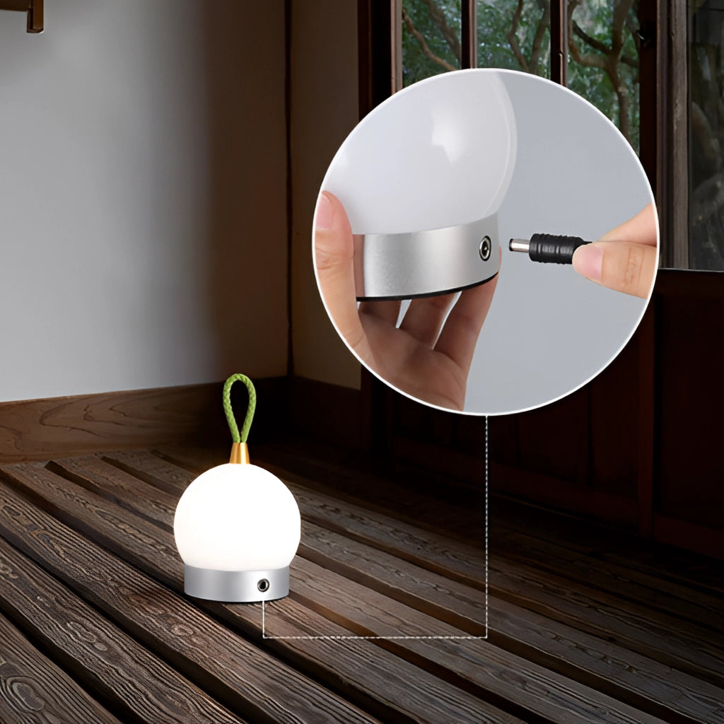 Waterproof cordless LED table lamp with orb design, placed on a wooden table against a neutral wall background.