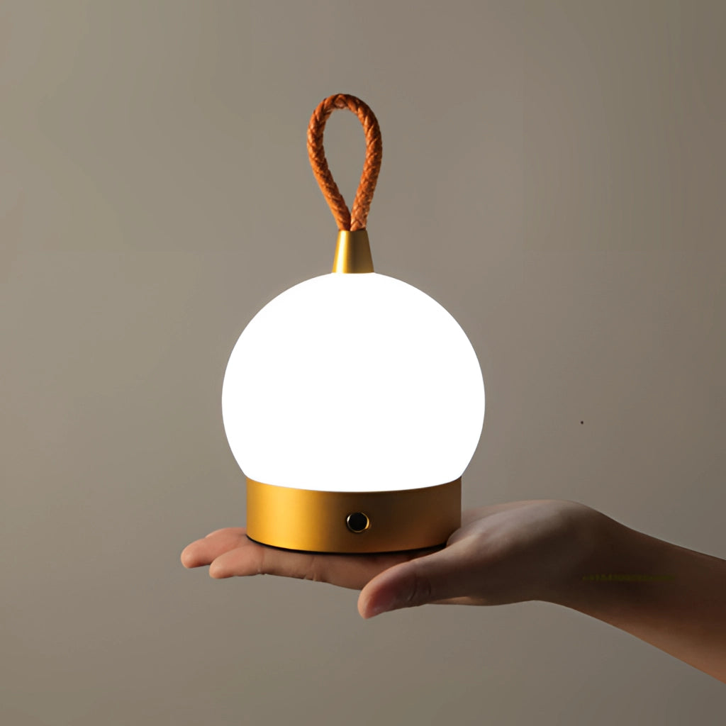A waterproof LED table lamp with a cordless orb design emitting a soft amber light, placed on a wooden surface.