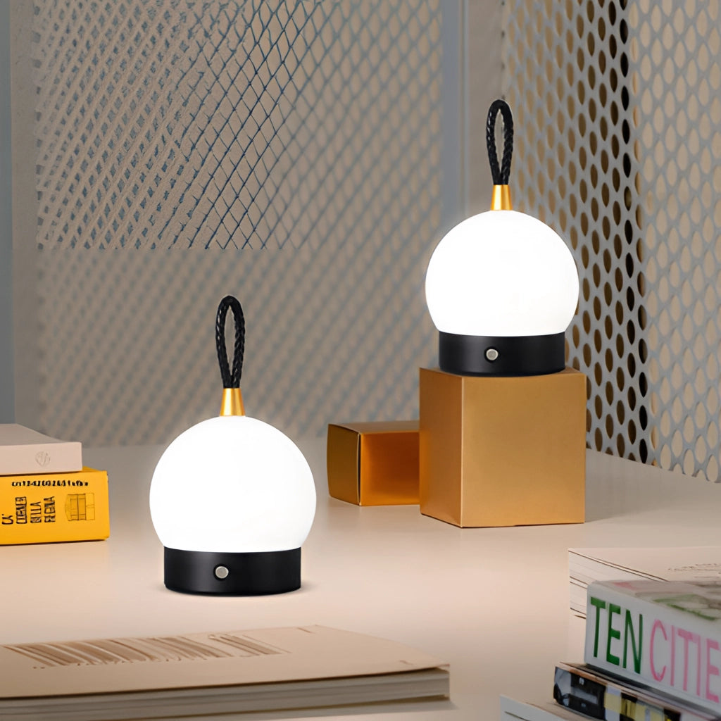 Waterproof LED table lamp in a cordless orb design, emitting warm light, displayed on a wooden surface.