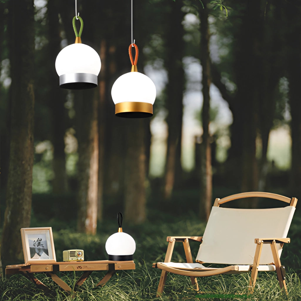Waterproof LED table lamp in a cordless orb design, placed on an outdoor table surrounded by grass and a chair, illuminated by sunlight.