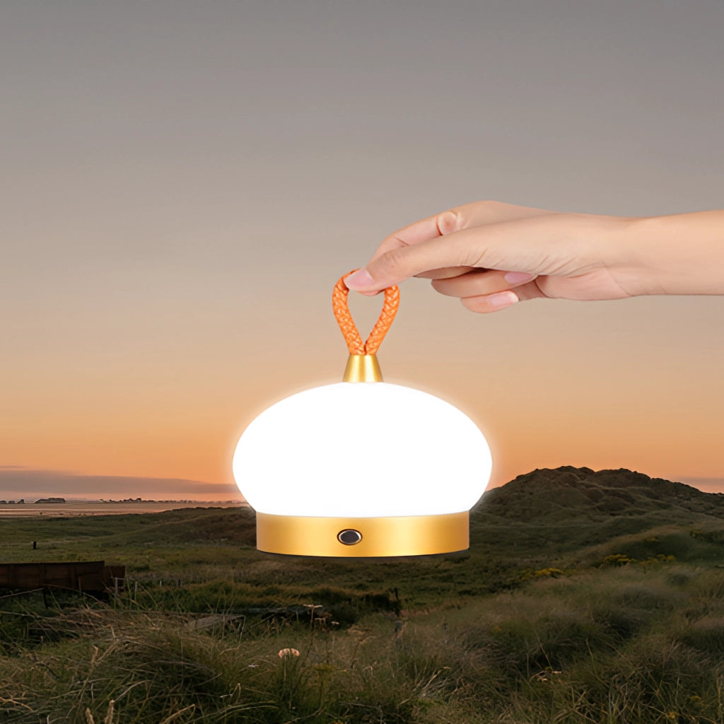 Waterproof LED table lamp with cordless orb design illuminated against a natural landscape backdrop during twilight.