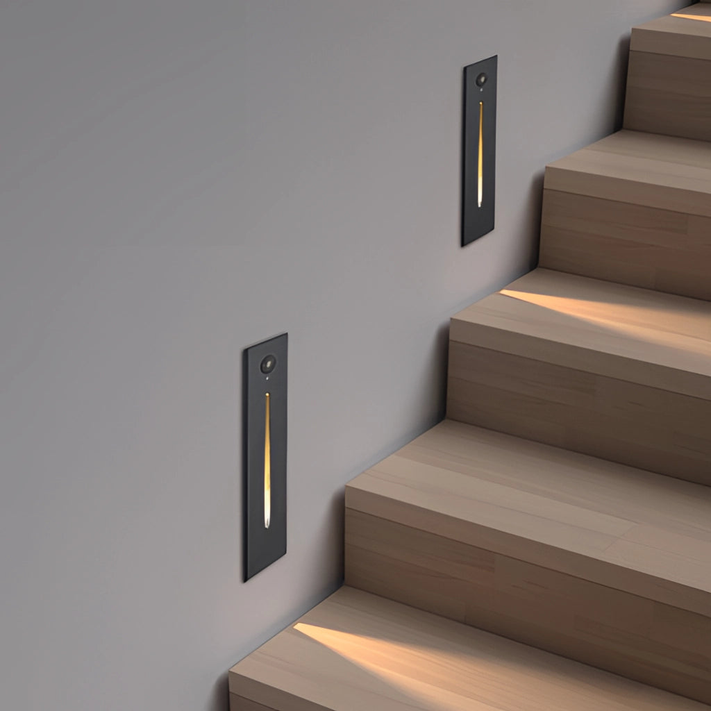 Modern black and white rectangular wall light illuminating a stylish indoor staircase area with grey hardwood floors and wooden shelving.