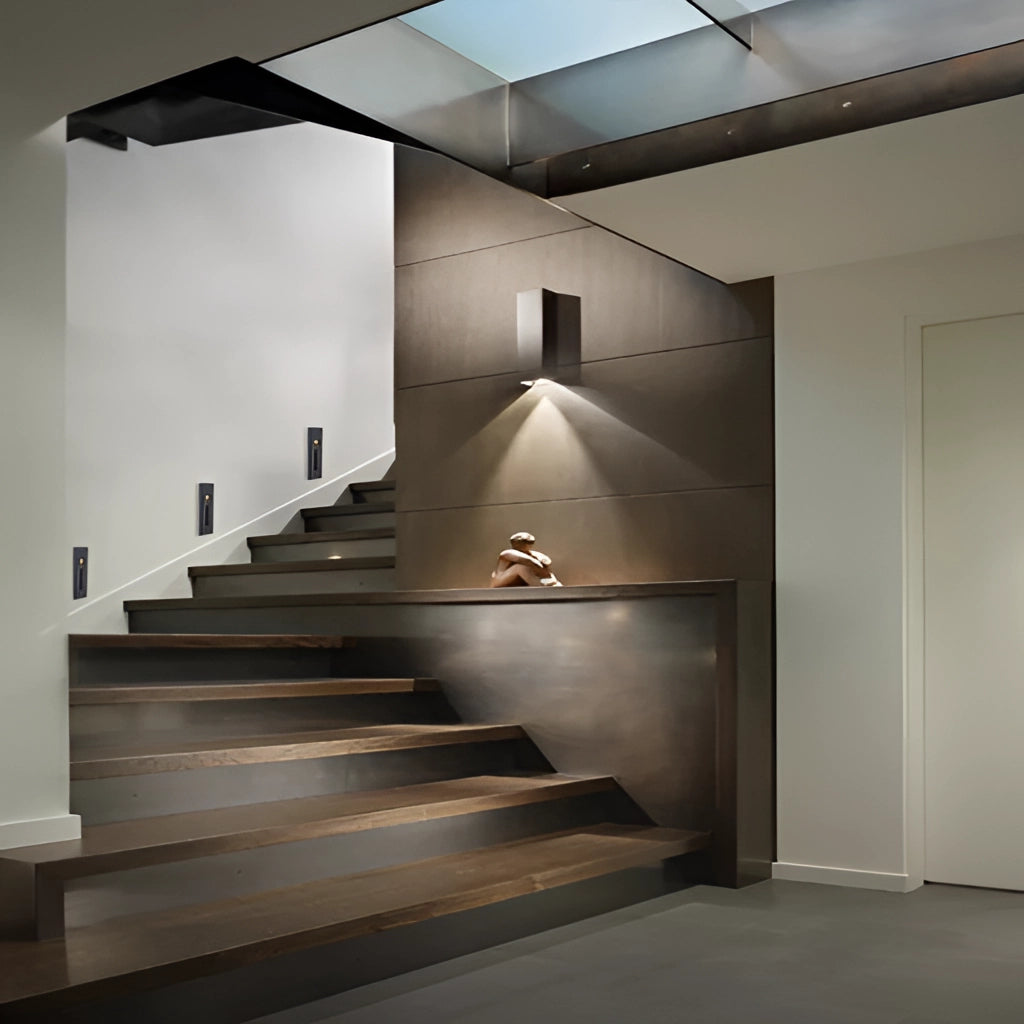 Modern ambient glow wall light mounted on an outdoor wall beside stairs, featuring a sleek black and white aluminum design, suitable for interior and exterior use.