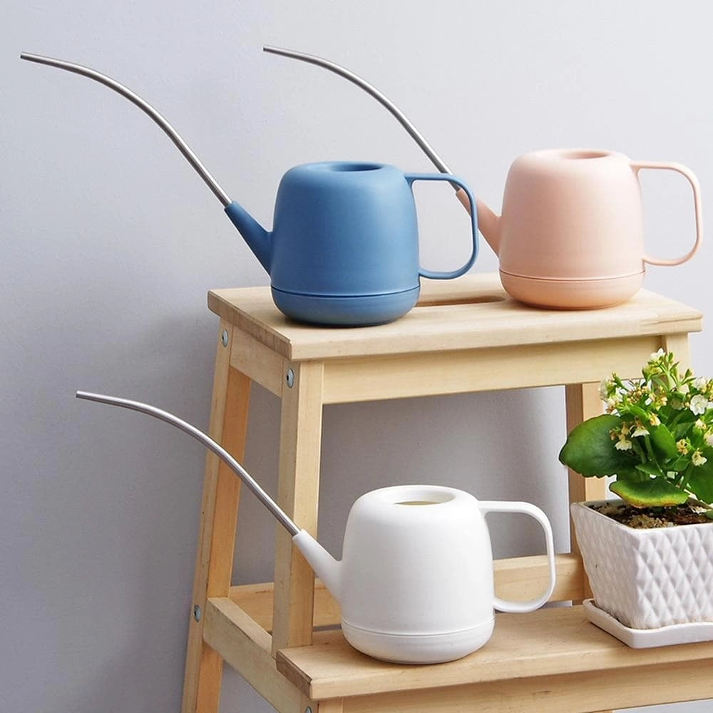 Modern and functional April Showers garden watering can placed on a wooden shelf next to houseplants and flowerpots.