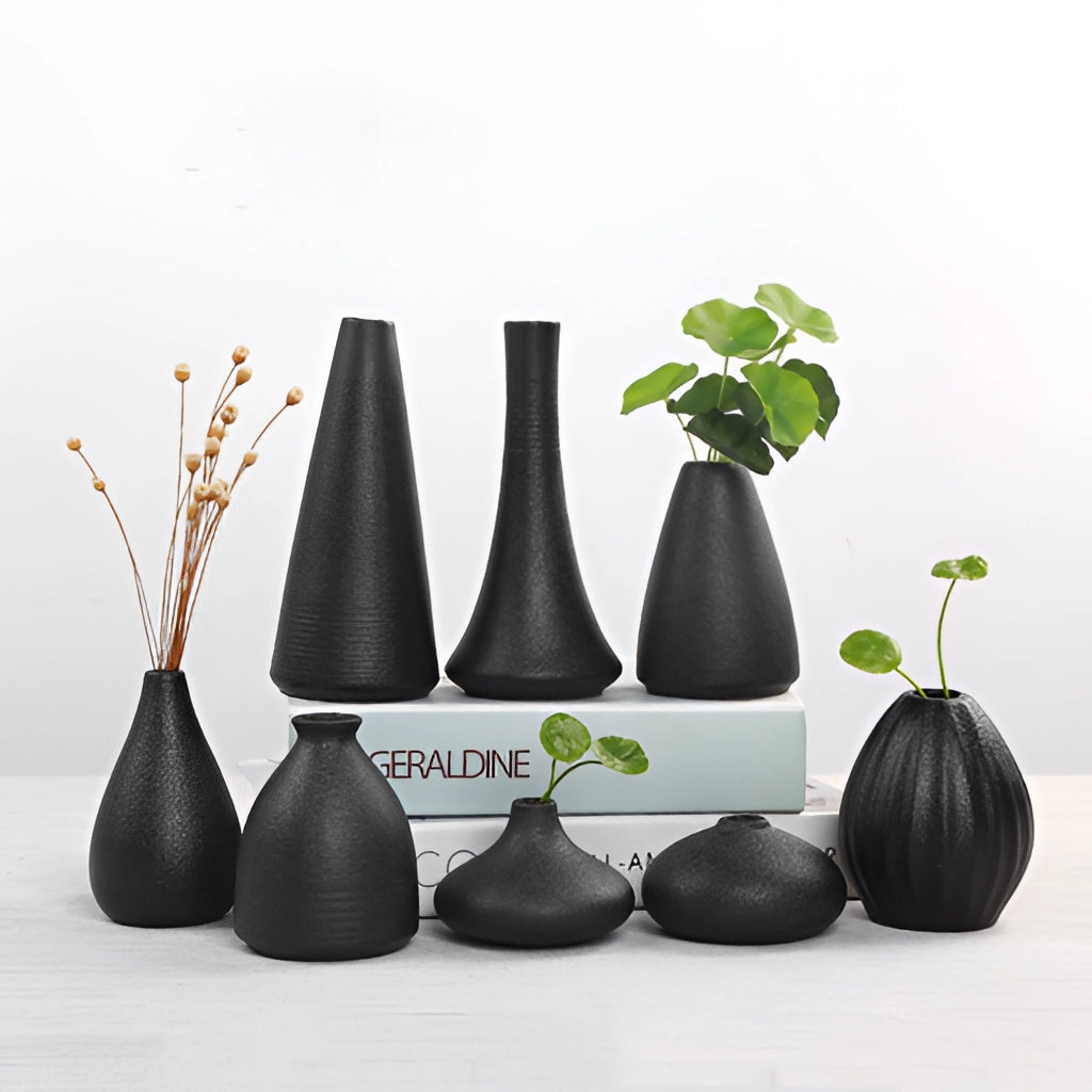 A black ceramic vase displayed in a home setting with wooden surfaces, featuring a creative arrangement of plants and artistic elements.