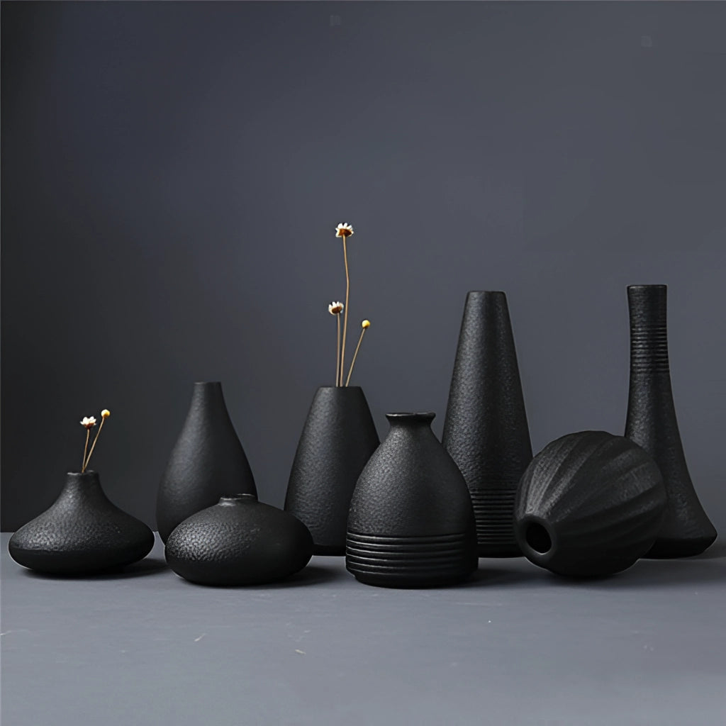 A black ceramic vase with a sleek cylindrical design, perfect for home and garden decor, showcased in a still life setting.