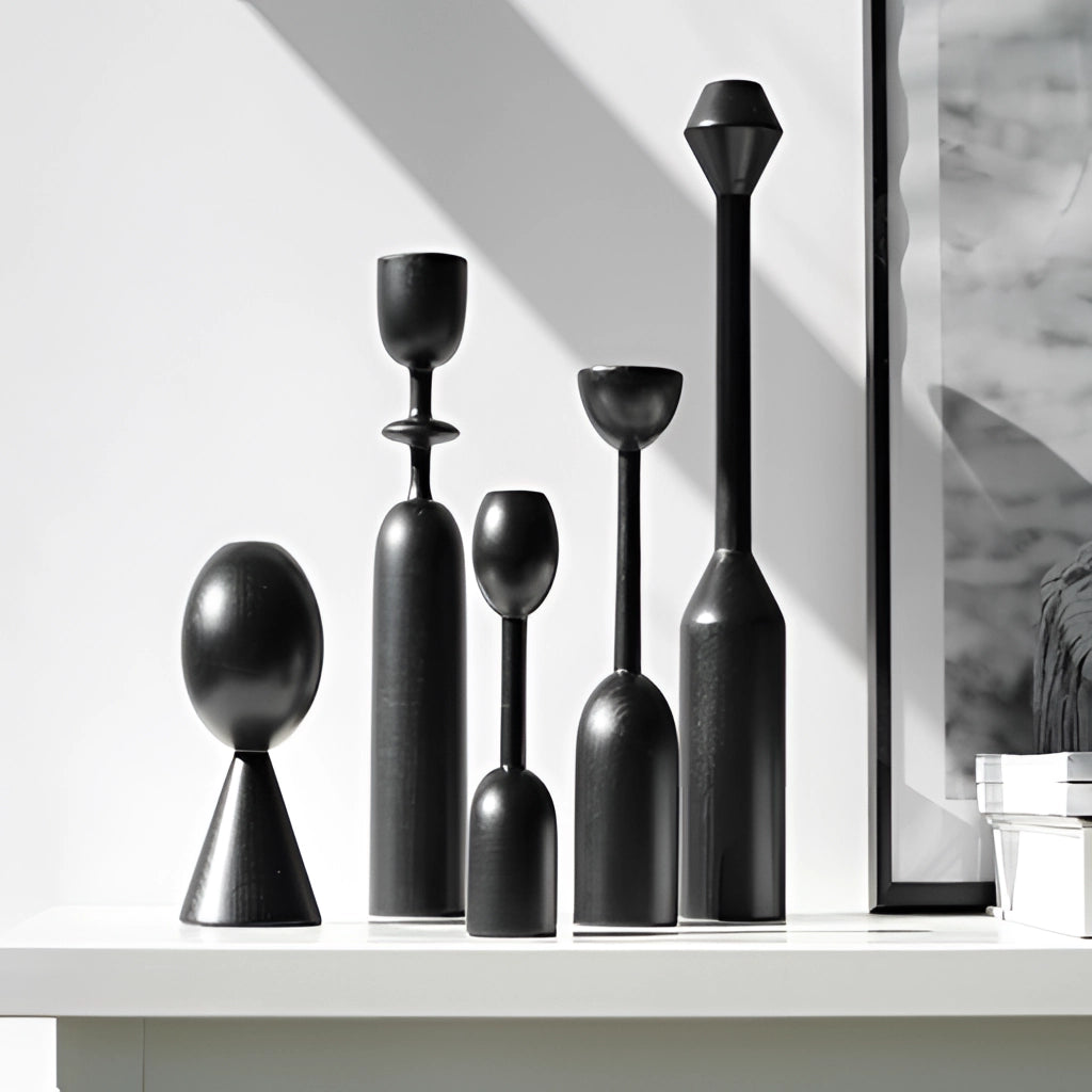 Set of black wooden candle holders arranged on a wooden shelf with houseplants and decorative glassware in the background.