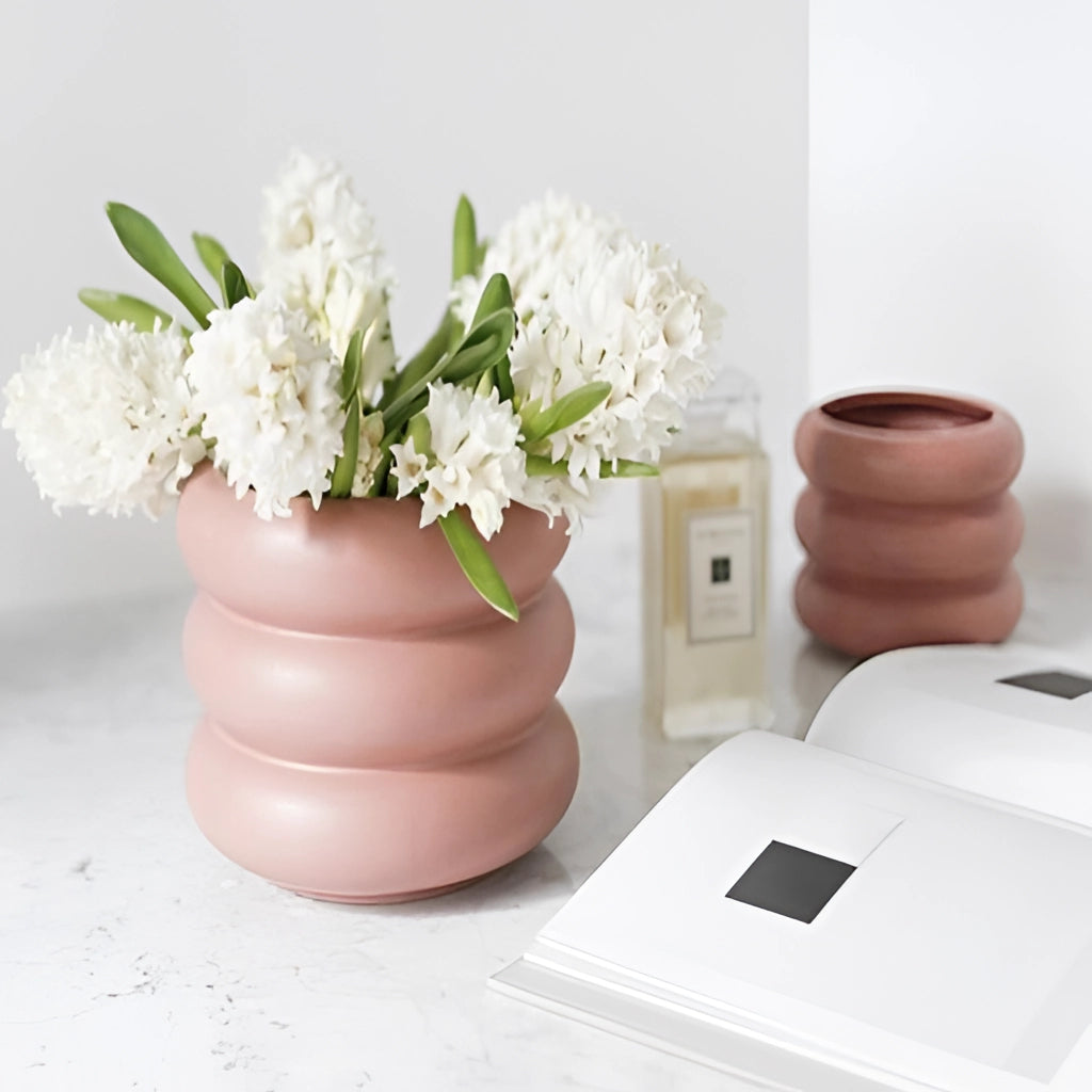 Ceramic round bubble glass planter vase with a white finish, holding a vibrant plant with green leaves and colorful flowers, placed on a table.