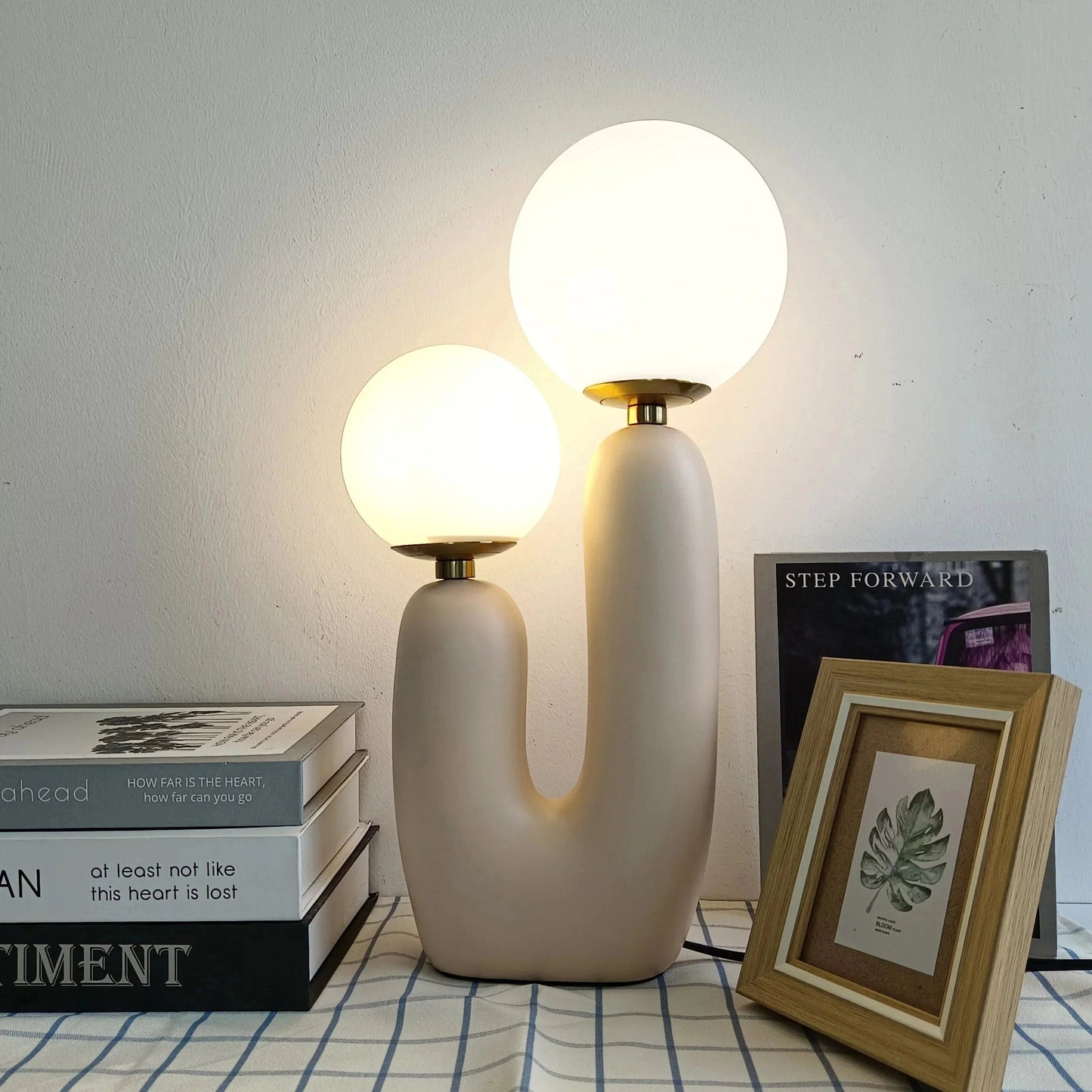 Cactus design table lamp with milk glass globes on a wooden base, featuring LED lighting, positioned on a wooden floor with interior design elements including a picture frame and ceiling details in the background.