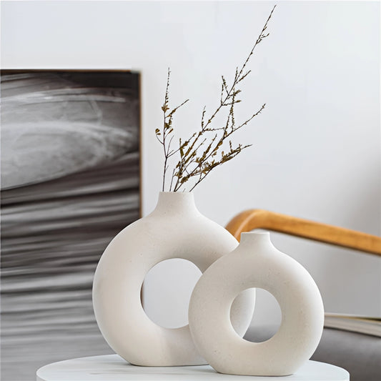 A ceramic donut-shaped vase for modern home decor placed on a wooden surface with twigs inside, showcasing creative arts and still life photography.
