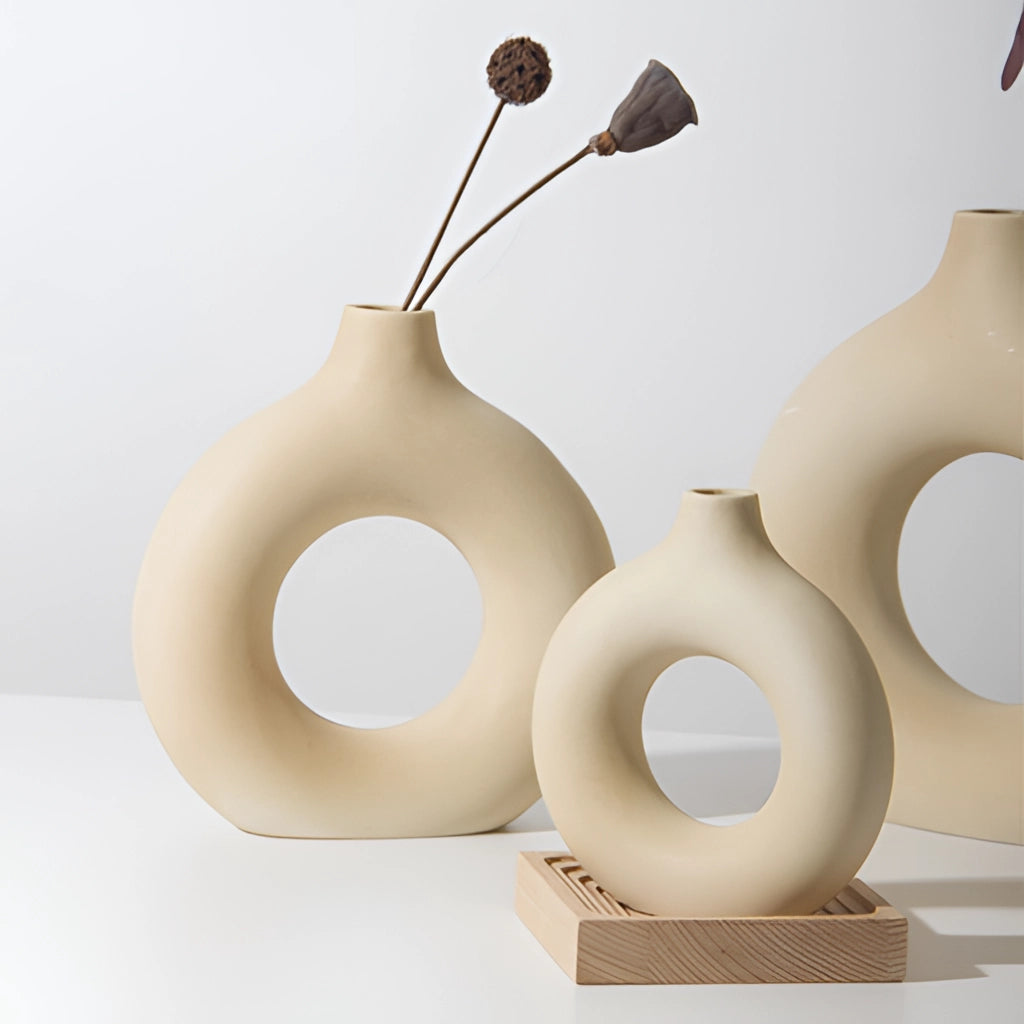 Ceramic donut shape vase displayed on a wooden surface with a twig inside, used for modern home decor.