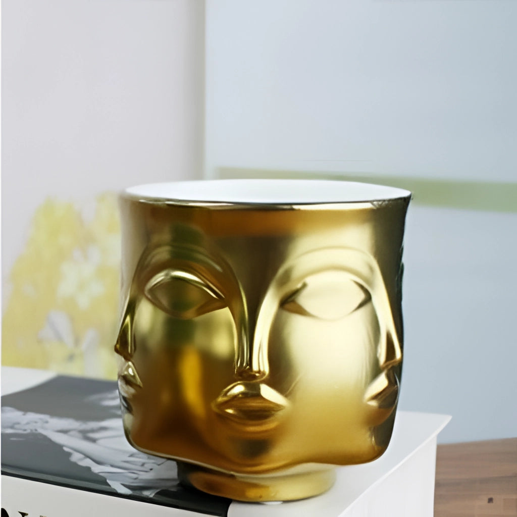 A gold ceramic flowerpot with a modern face design, ideal for succulents.