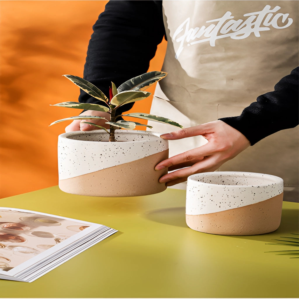 A set of small, medium, and large ceramic flowerpots in linen color placed on a table.