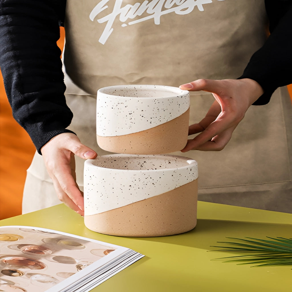 A person holding a white ceramic flowerpot with a yellow sleeve in a hand.