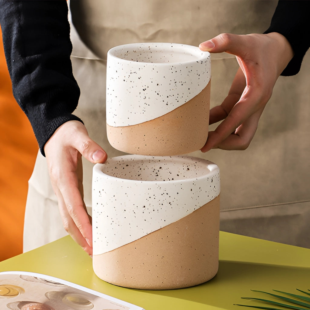 A person's hand holding a small ceramic flowerpot in a linen color.