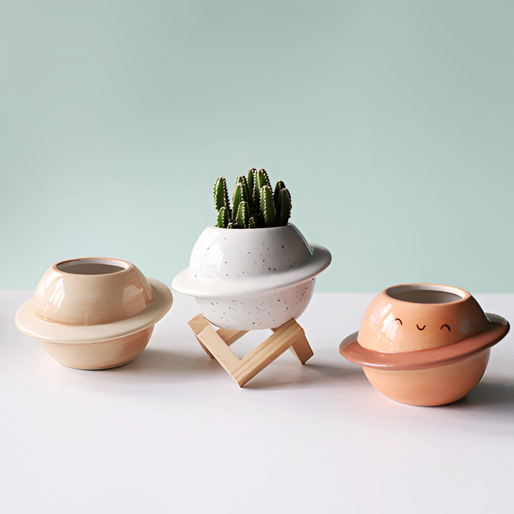 Ceramic Planet Plant Pot with Astral Galaxy Design, featuring a round porcelain shape with blue and white celestial patterns, displayed on a wooden surface with a plant inside.